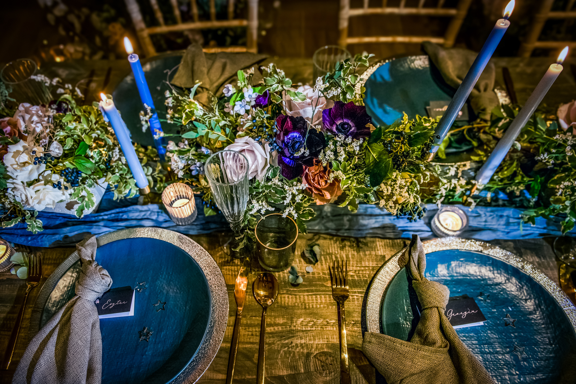 Overhead view of celestial-inspired place settings with blue plates, wild florals, and glowing candles.