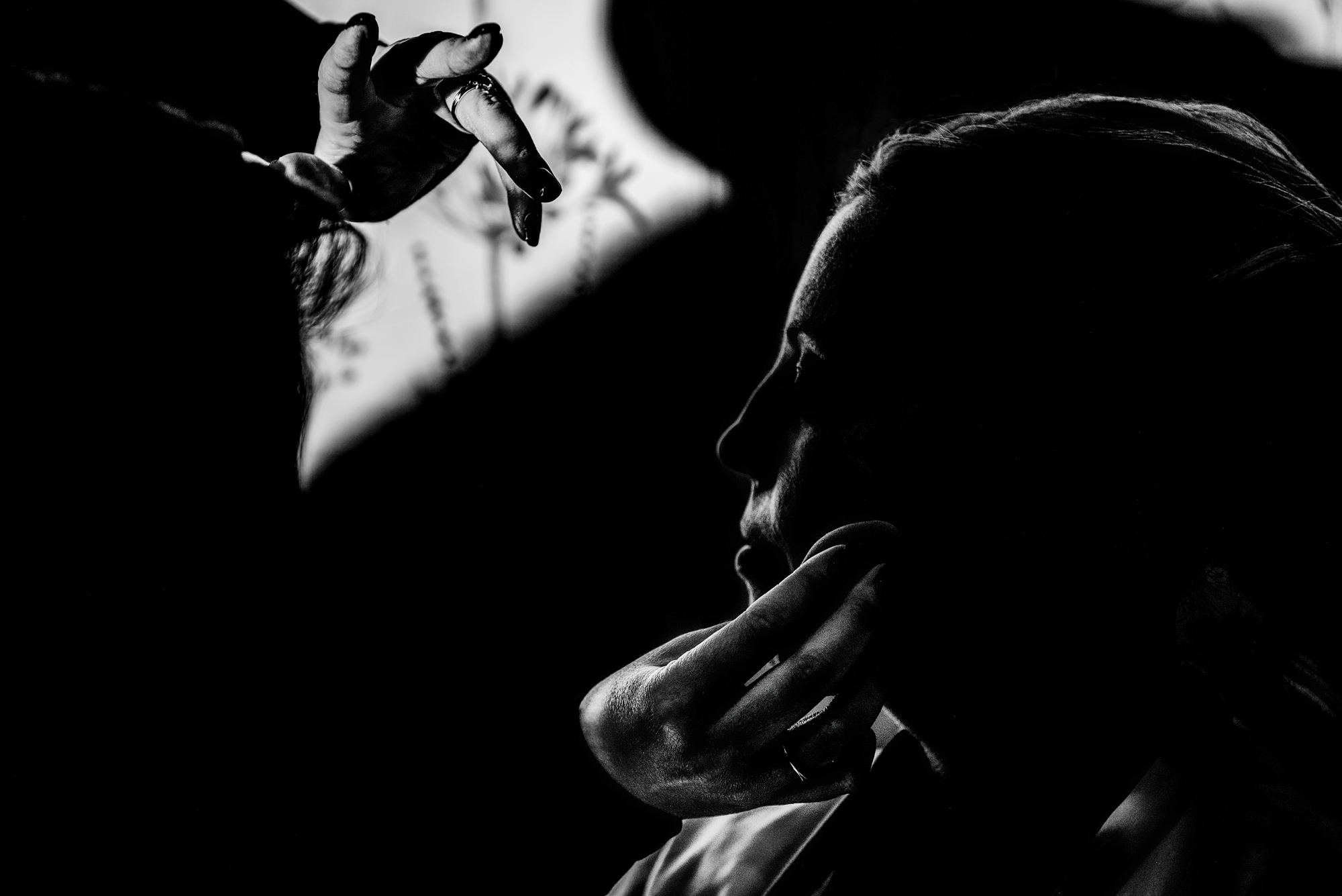 Delicate silhouette of a makeup artist shaping the bride’s face in dramatic light.