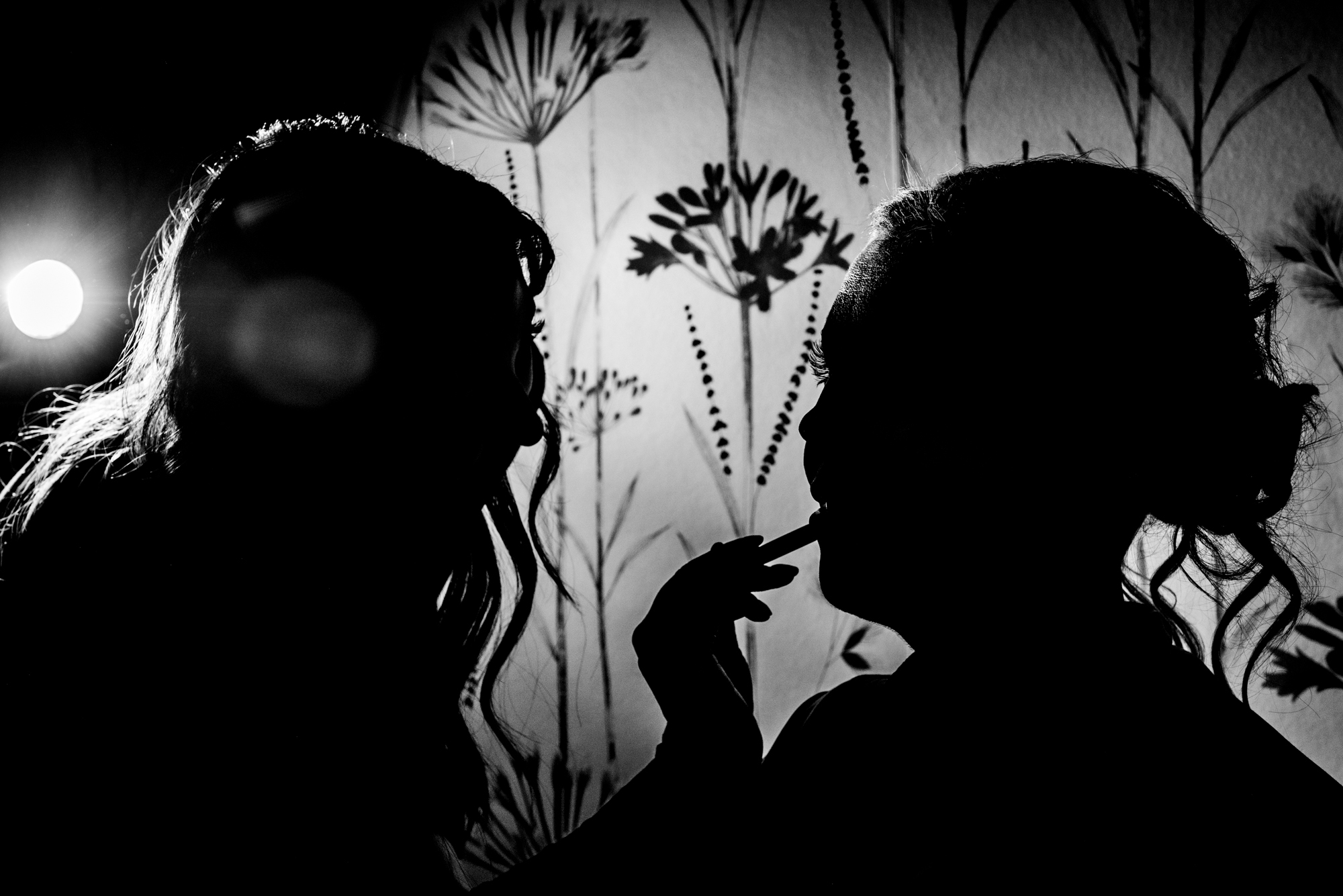 Silhouetted moment of lipstick being applied against patterned wallpaper.