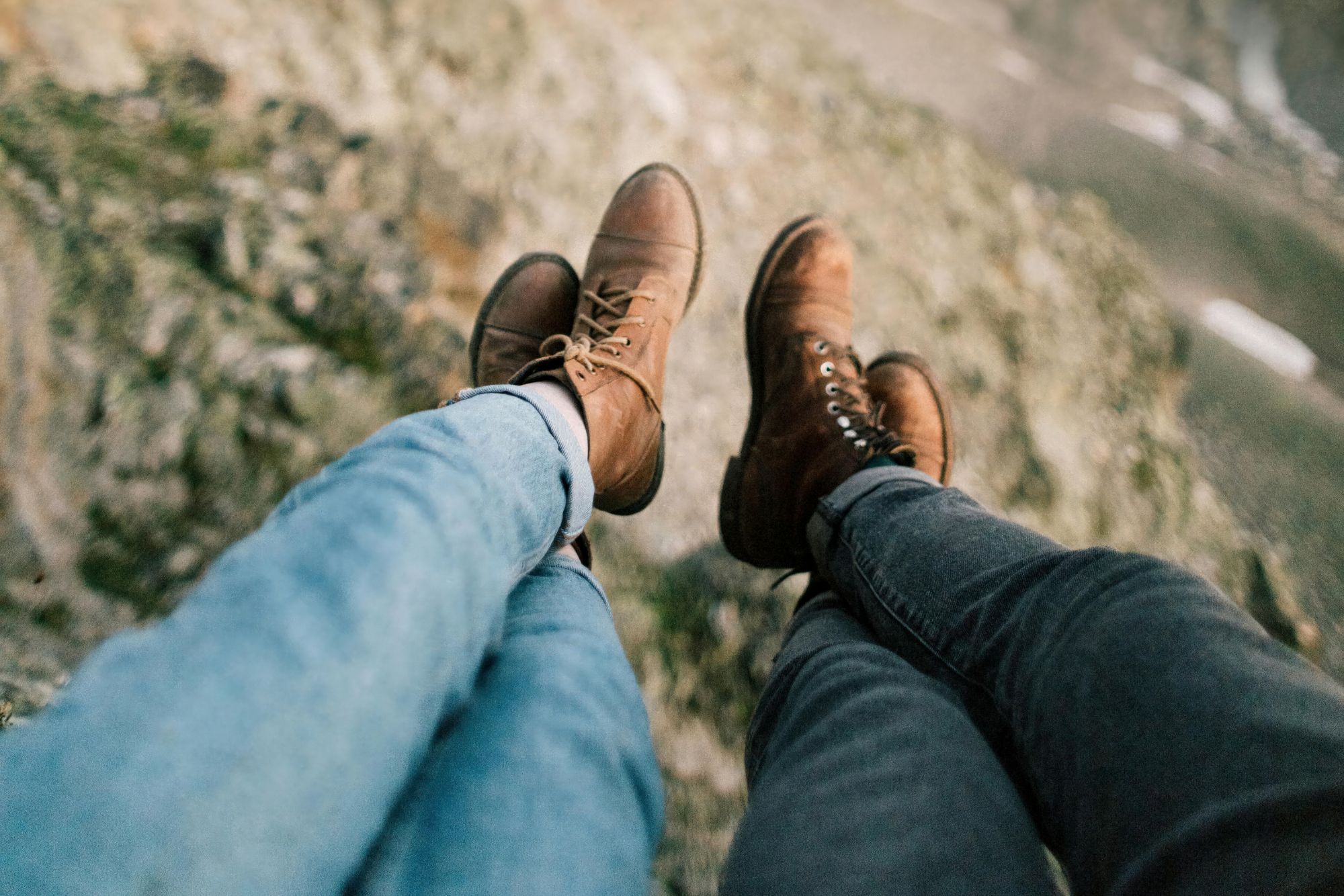 Couple sitting on a cliff edge with hiking boots during an adventurous outdoor couple photoshoot.