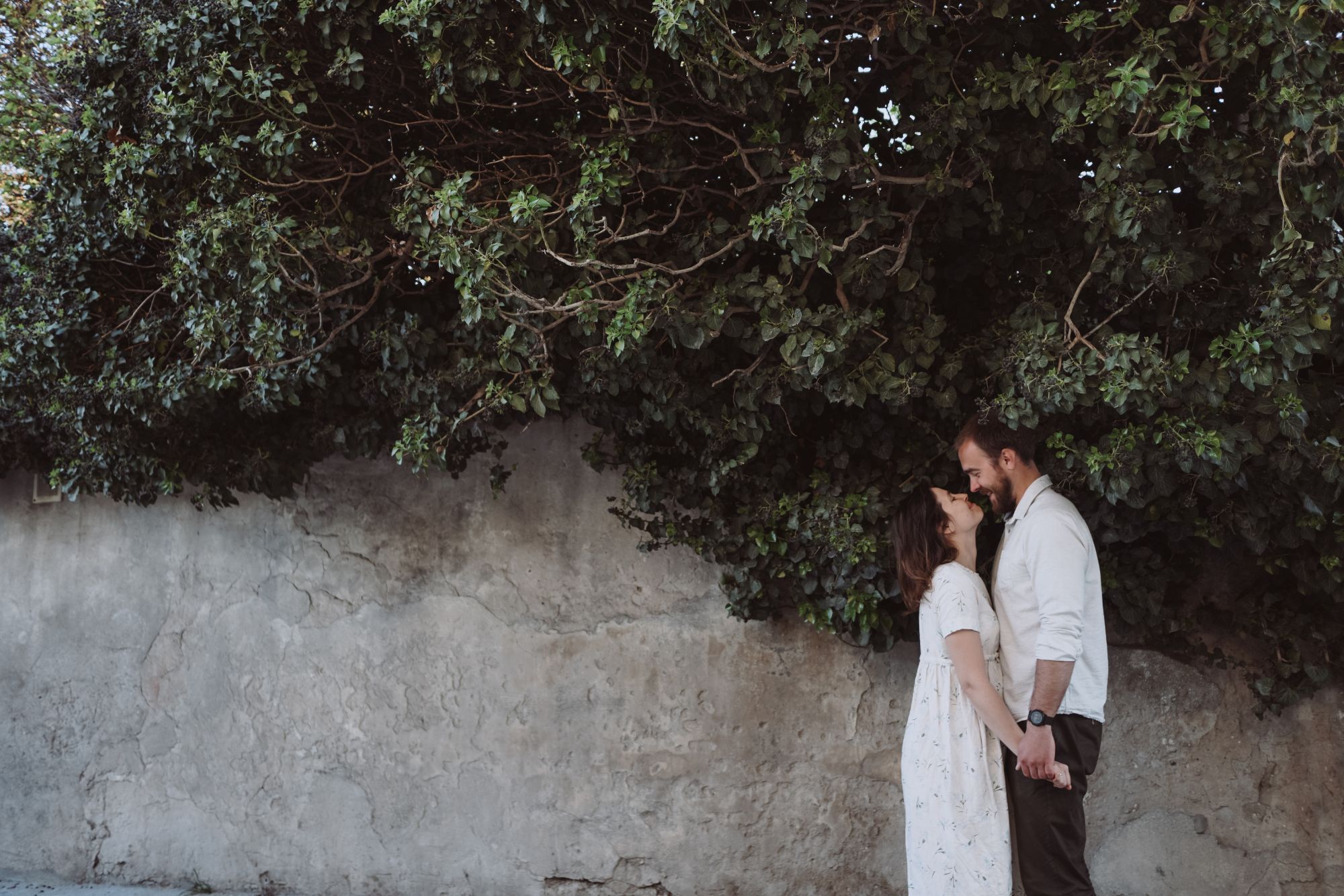 Couple standing together beneath lush greenery during a romantic outdoor couple photoshoot.