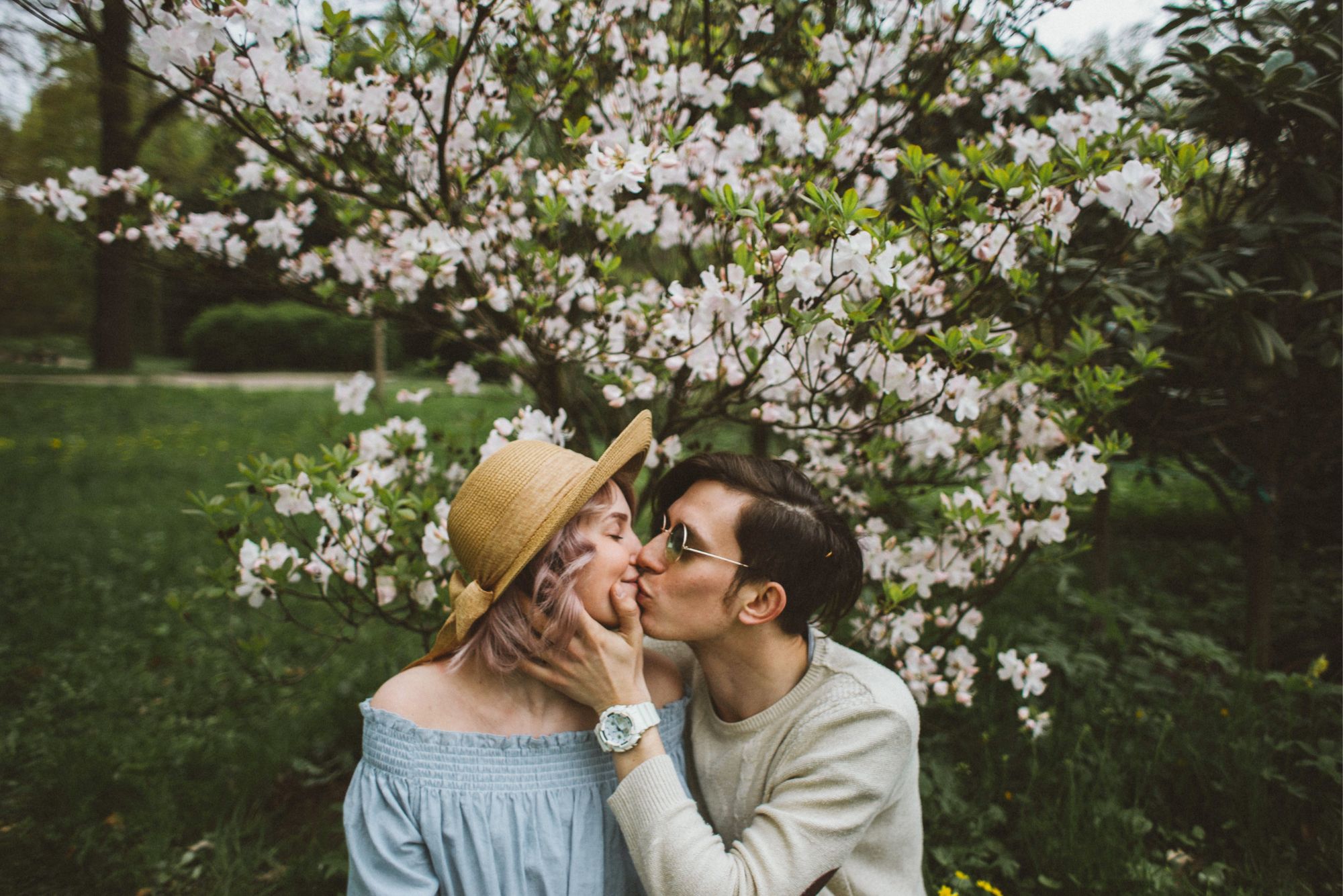 Couple kissing beneath blooming spring flowers during a relaxed outdoor couple photoshoot in a garden.