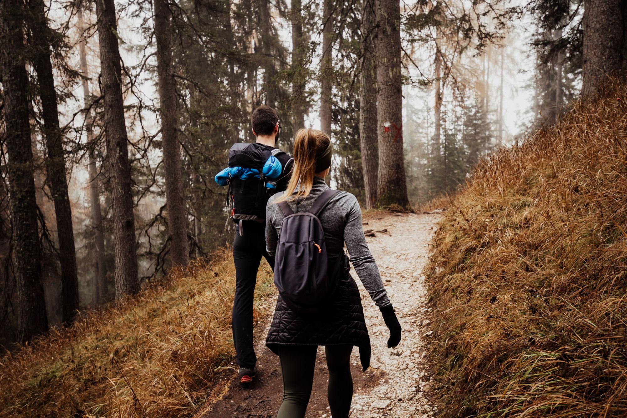 Couple hiking together through a forest trail during an adventurous outdoor couple photoshoot.