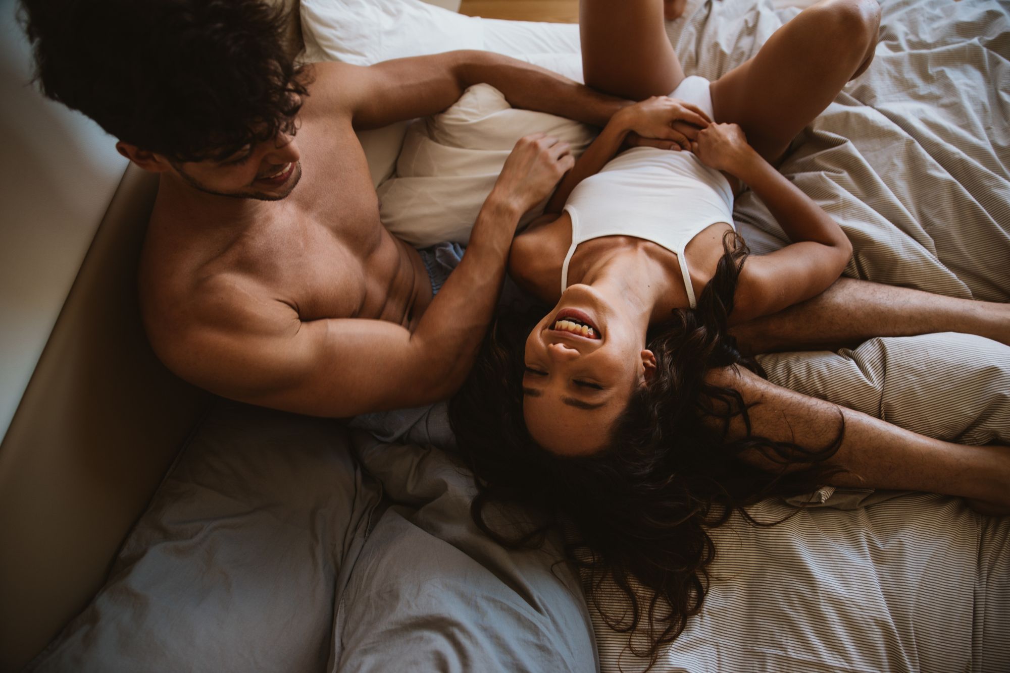 Couple laughing together on a bed during a relaxed at-home lifestyle couple photoshoot.