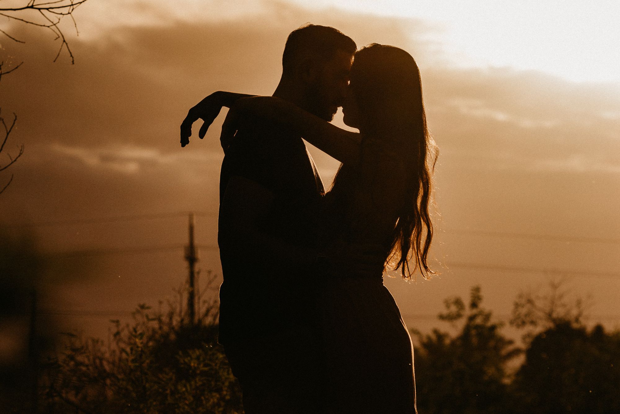 Silhouetted couple embracing at sunset during a romantic outdoor couple photoshoot.