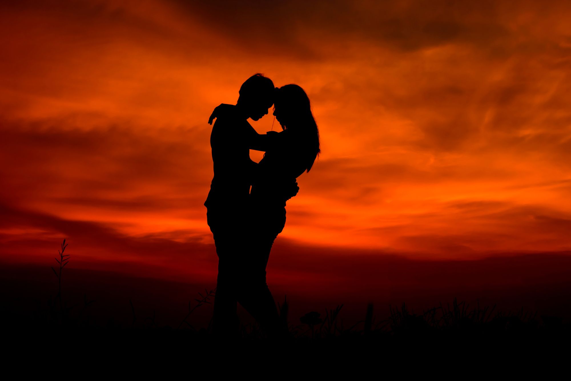 Couple holding each other against a dramatic orange sunset sky during an evening couple photoshoot.