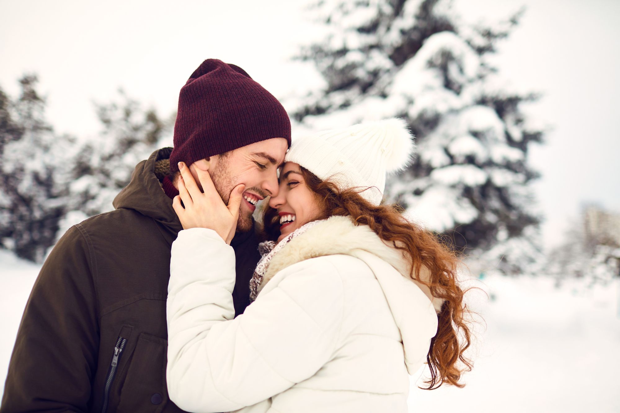 Couple smiling closely together during a winter couple photoshoot in snowy landscape.