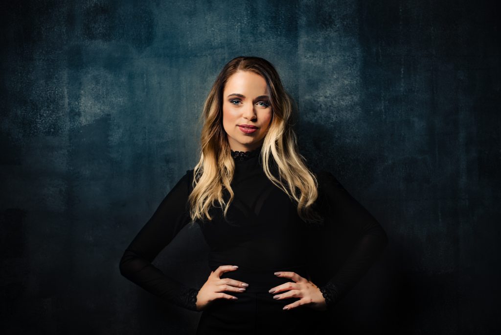 Confident studio portrait session with a woman standing against a dark textured wall.
