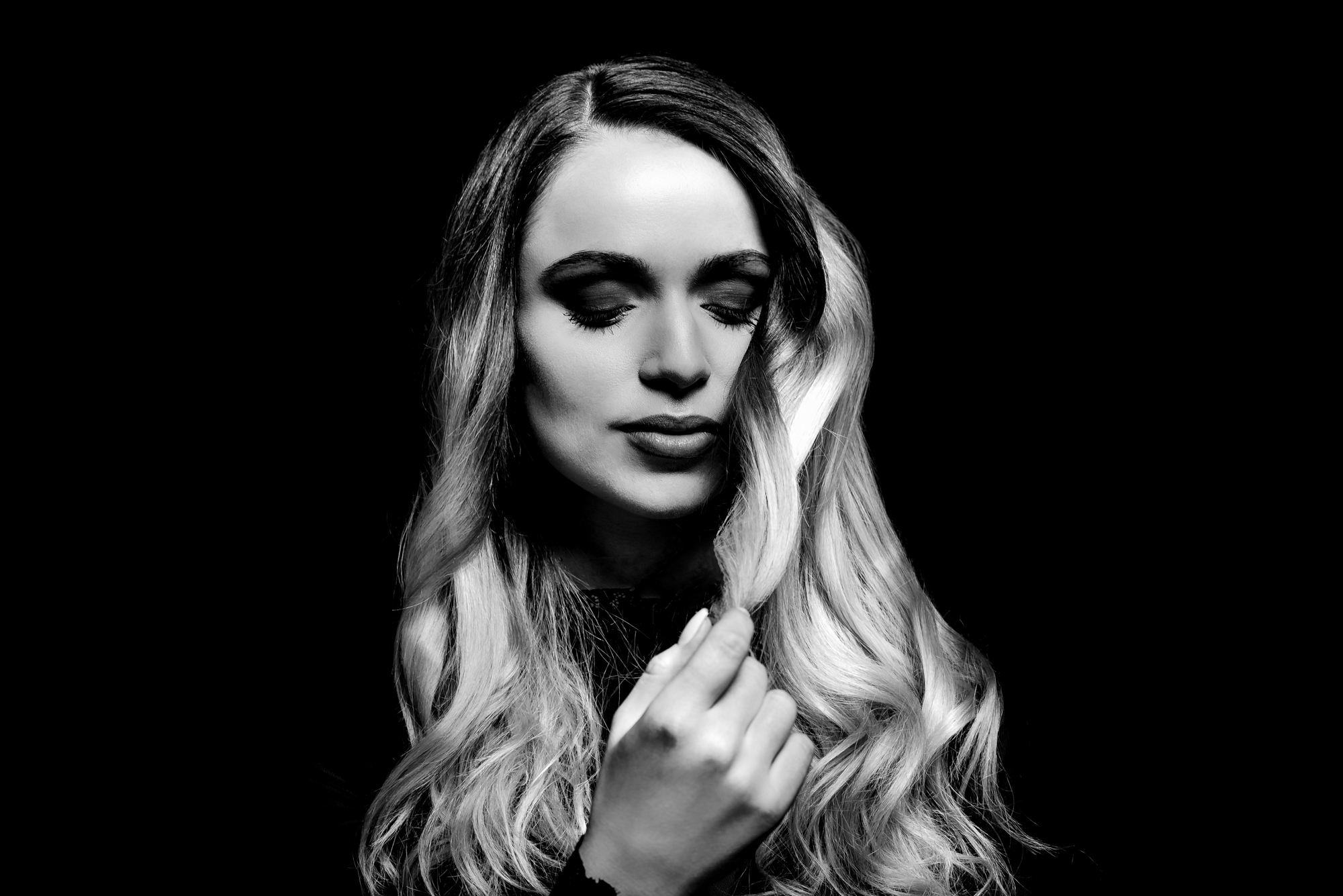 Black and white studio portrait with eyes closed against a dark background.