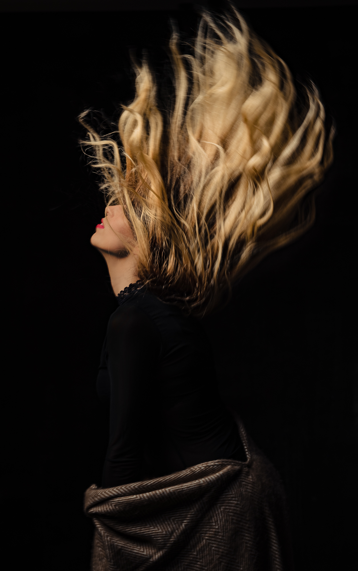 Creative studio portrait with a woman flipping her hair in dramatic motion.