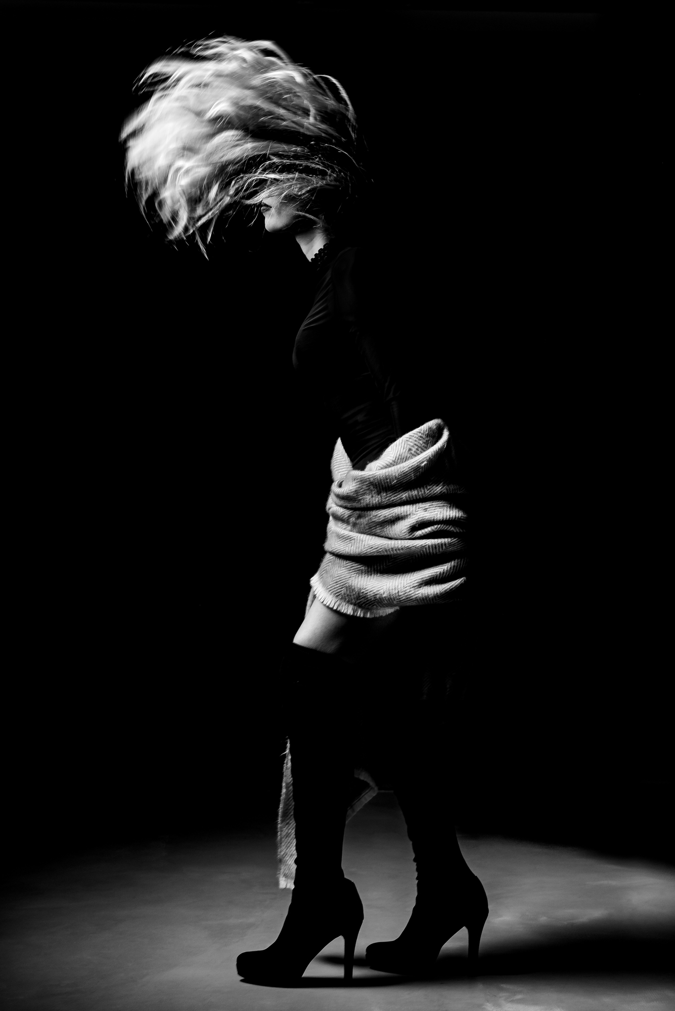 Black and white studio portrait of a woman with moving hair and strong shadow.