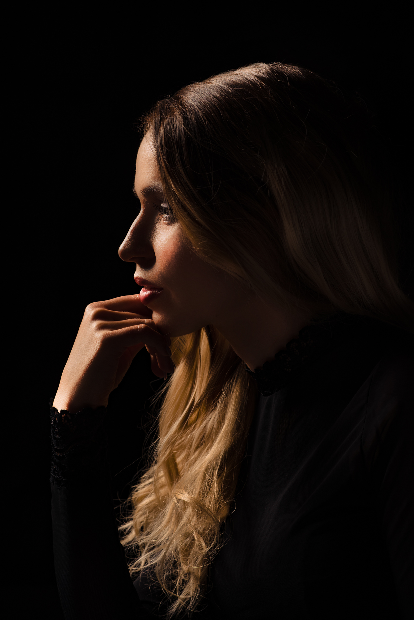 Low-key studio portrait in profile against a black background.