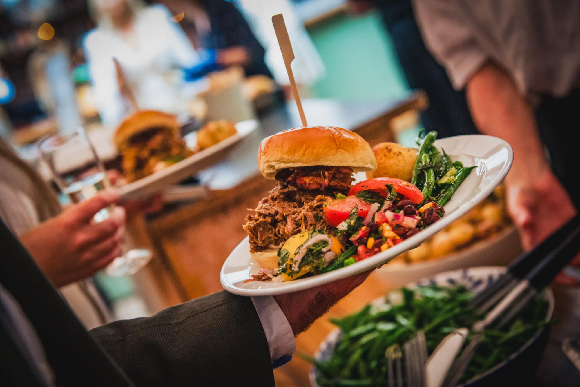 Pulled pork burger and salad served during relaxed wedding reception dining with guests mingling.