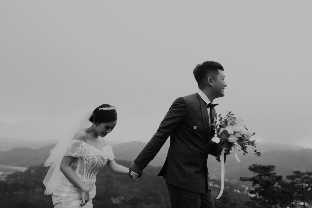 Bride and groom holding hands while walking across misty hillside, laughing together after their ceremony.