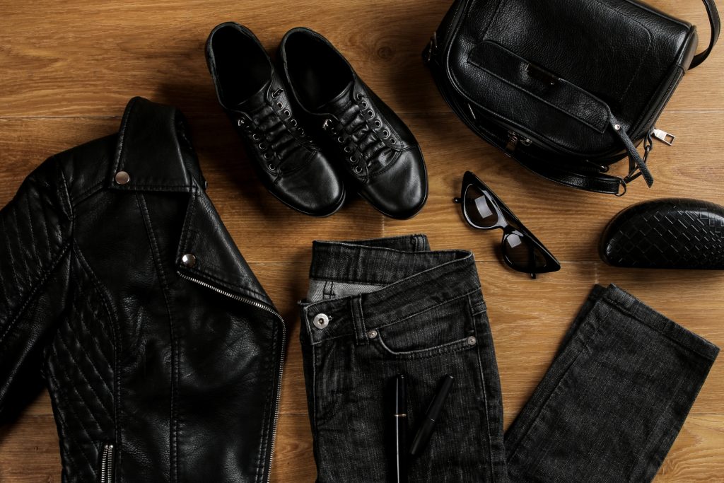 Black leather jacket, dark jeans, trainers and bag arranged as practical photographer outfit flat lay.
