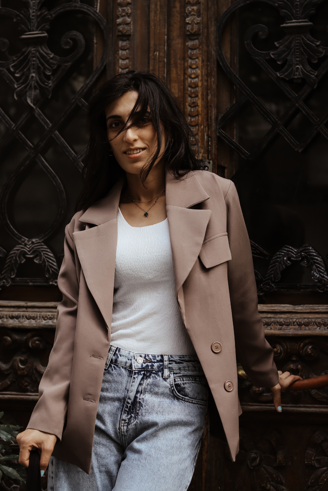 Woman wearing blazer and jeans standing by ornate doorway, example of smart casual photographer outfit.
