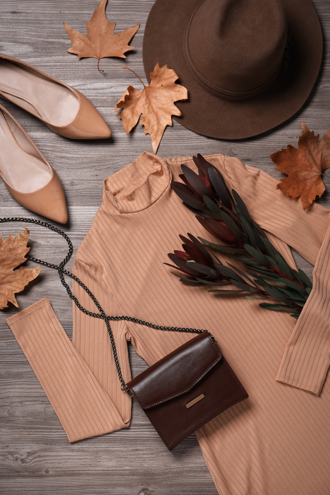 Neutral autumn outfit with hat, flats and beige top styled with seasonal accessories on wooden surface.