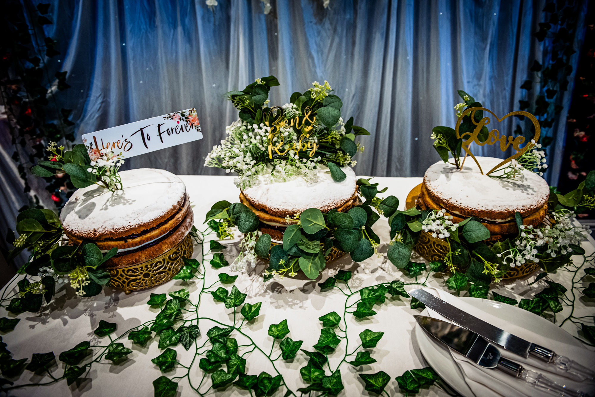 Rustic wedding cake display with greenery and personalised toppers at Arnos Manor Bristol venue.
