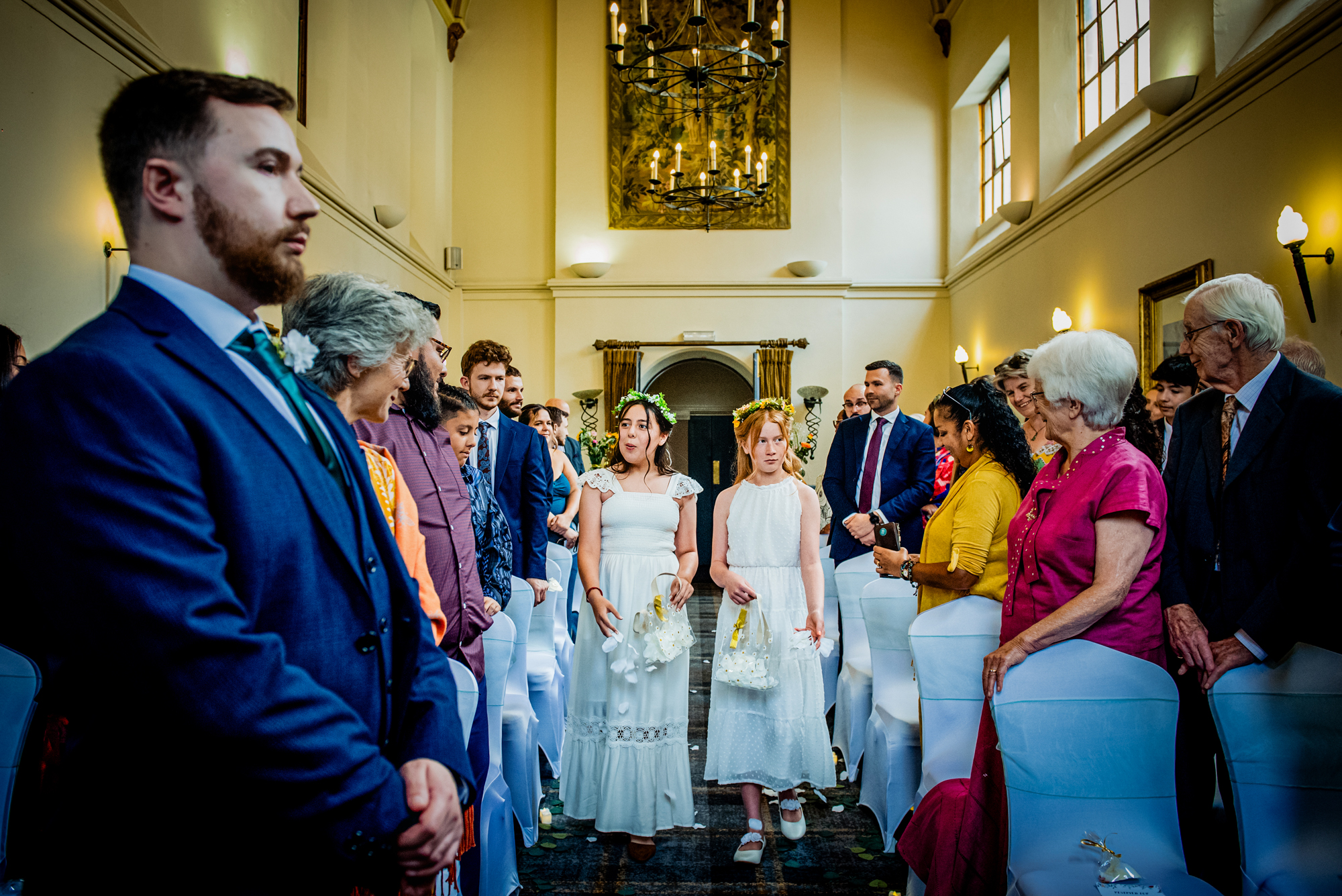 Flower girls walking down the aisle smiling during multicultural wedding ceremony at Arnos Manor Hotel Bristol.