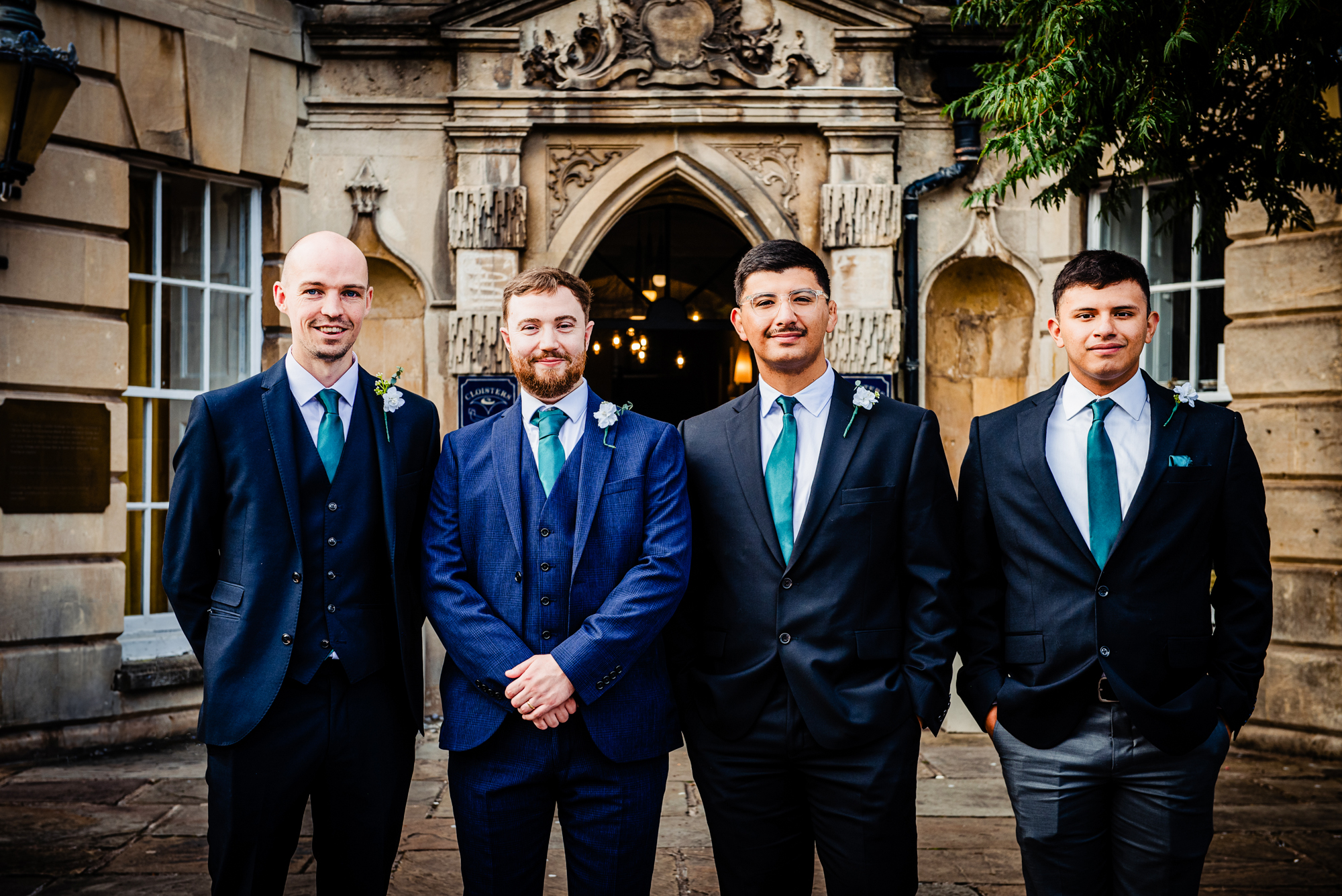 Groom and groomsmen in suits posing outside Arnos Manor Hotel entrance.