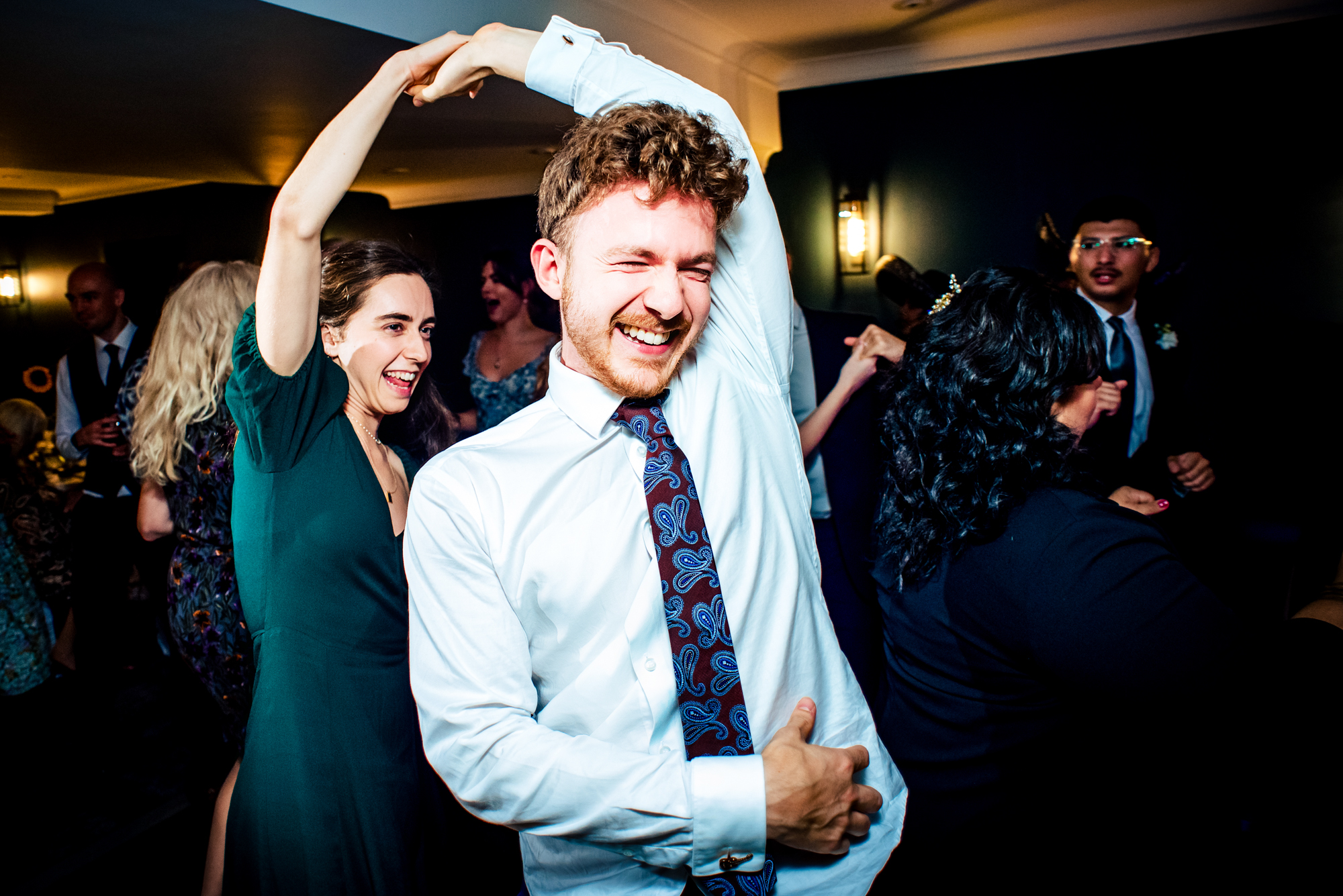 Guest dancing with arms raised, smiling widely on busy wedding dance floor.