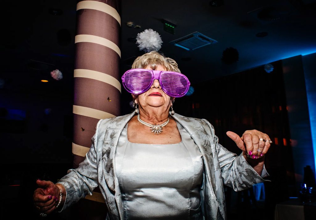 Grandmother wearing oversized purple glasses dancing at reception.