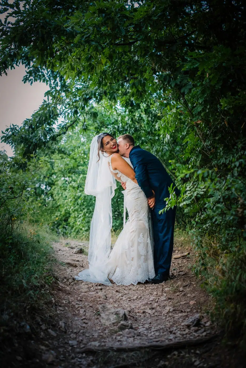 Bride and groom embracing on woodland path captured through documentary style wedding photography.