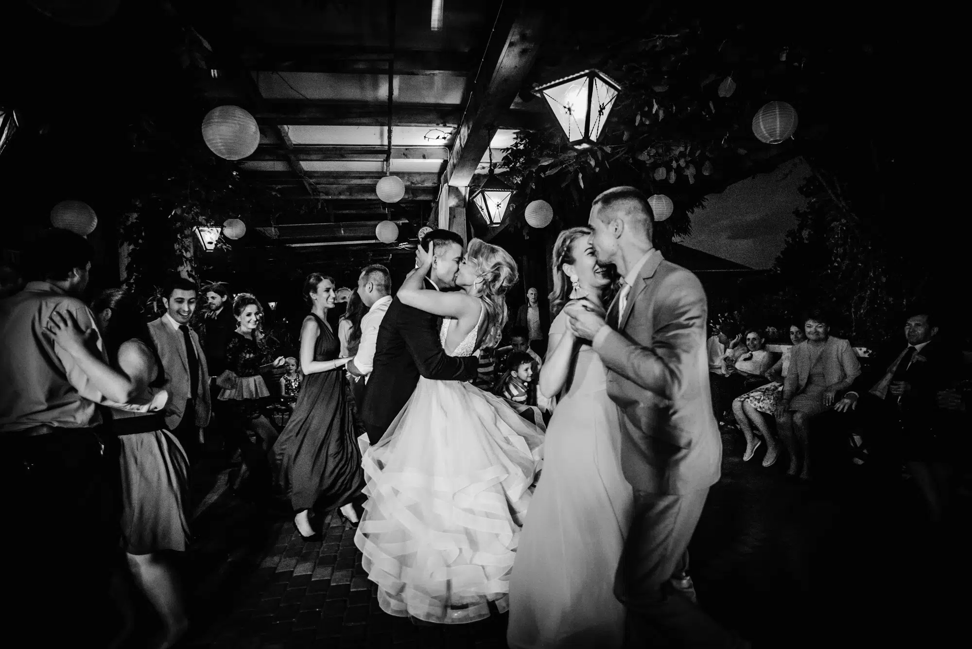 Guests dancing under lantern lights during wedding reception.