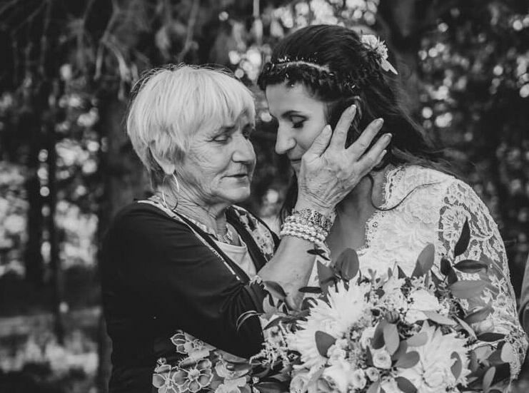 Elderly woman gently touching bride’s face during emotional outdoor ceremony.
