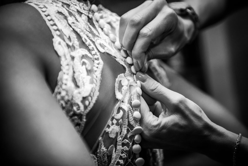 Hands fastening buttons on lace wedding dress, detailed preparation moment before ceremony.