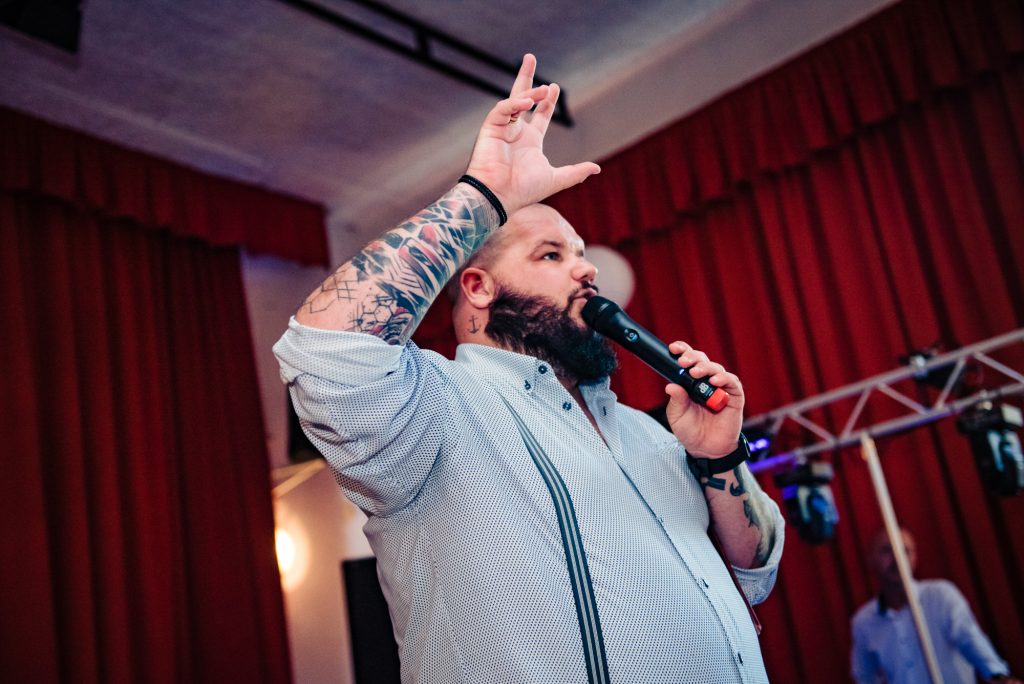 Wedding MC speaking into microphone during lively reception with red backdrop