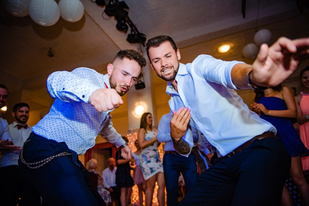 Groom's friends dancing and pointing toward camera during lively wedding reception.