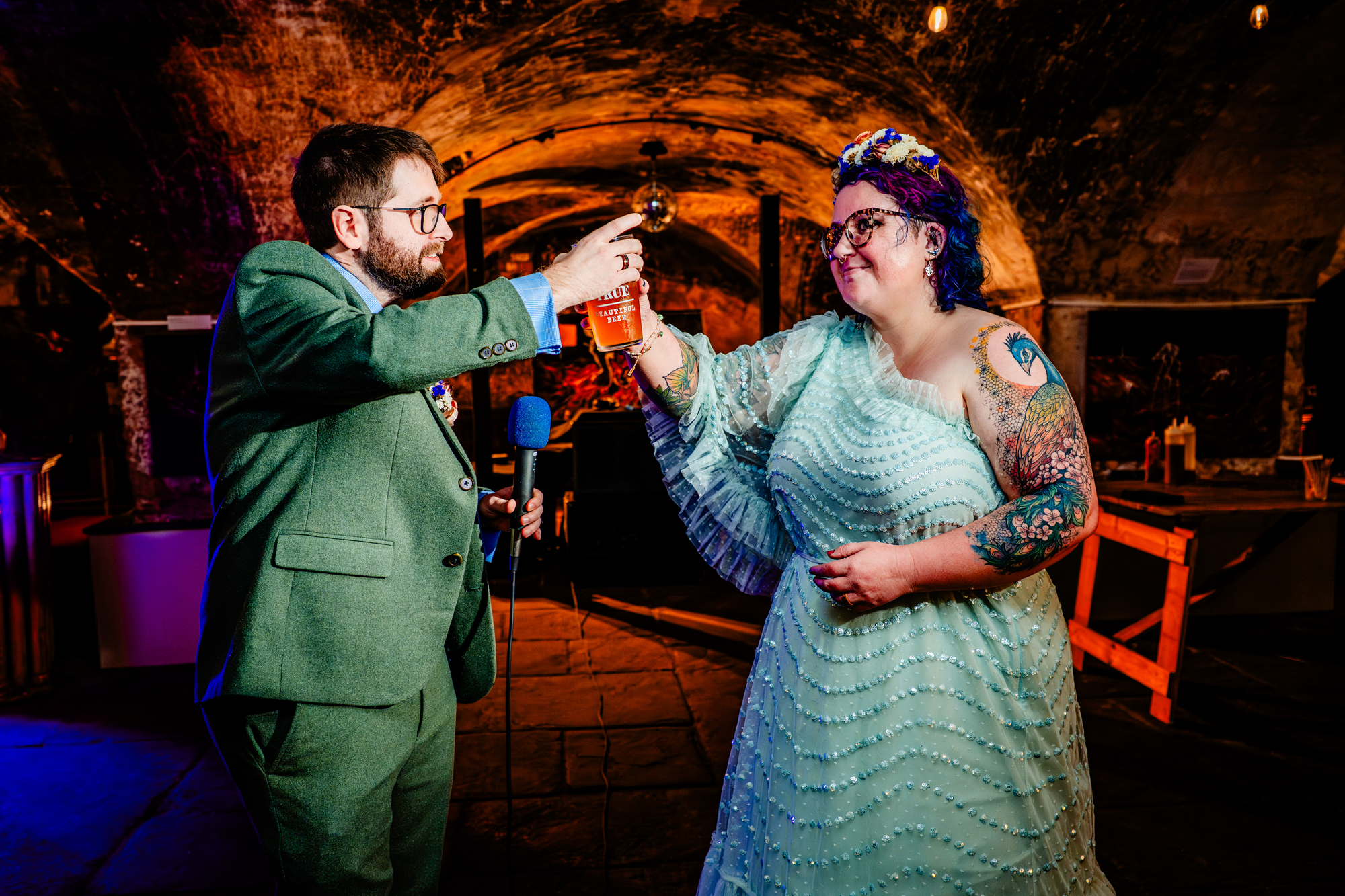 Couple clinks drinks together in a celebratory toast under colourful event lighting.