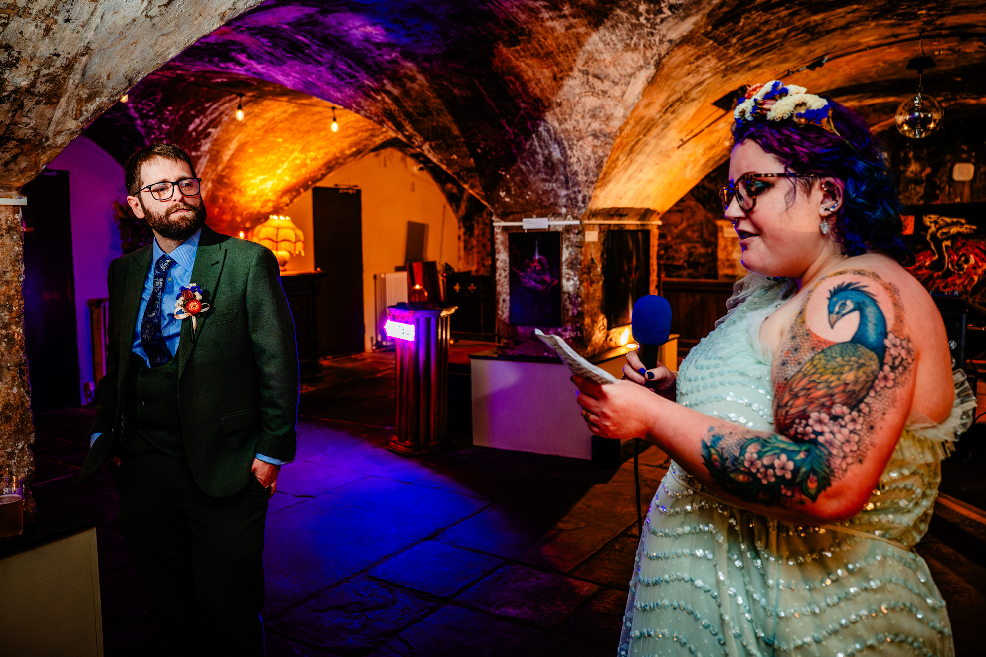 Corrie with microphone addresses the room while the groom listen attentively in the background.