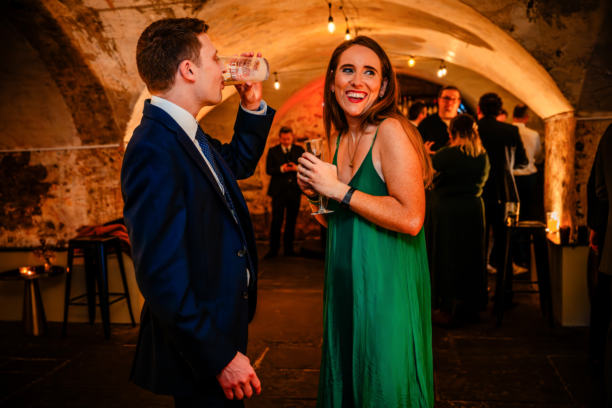 Two guests chat and drink, smiling at each other in a softly lit reception space.