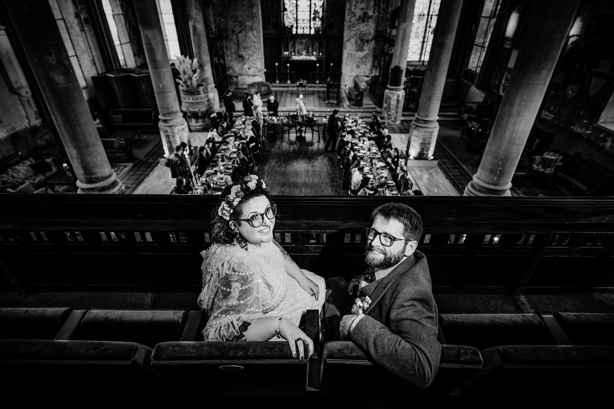 Newlyweds seated on a balcony smile at the camera while guests dine below at The Mount Without in Bristol.
