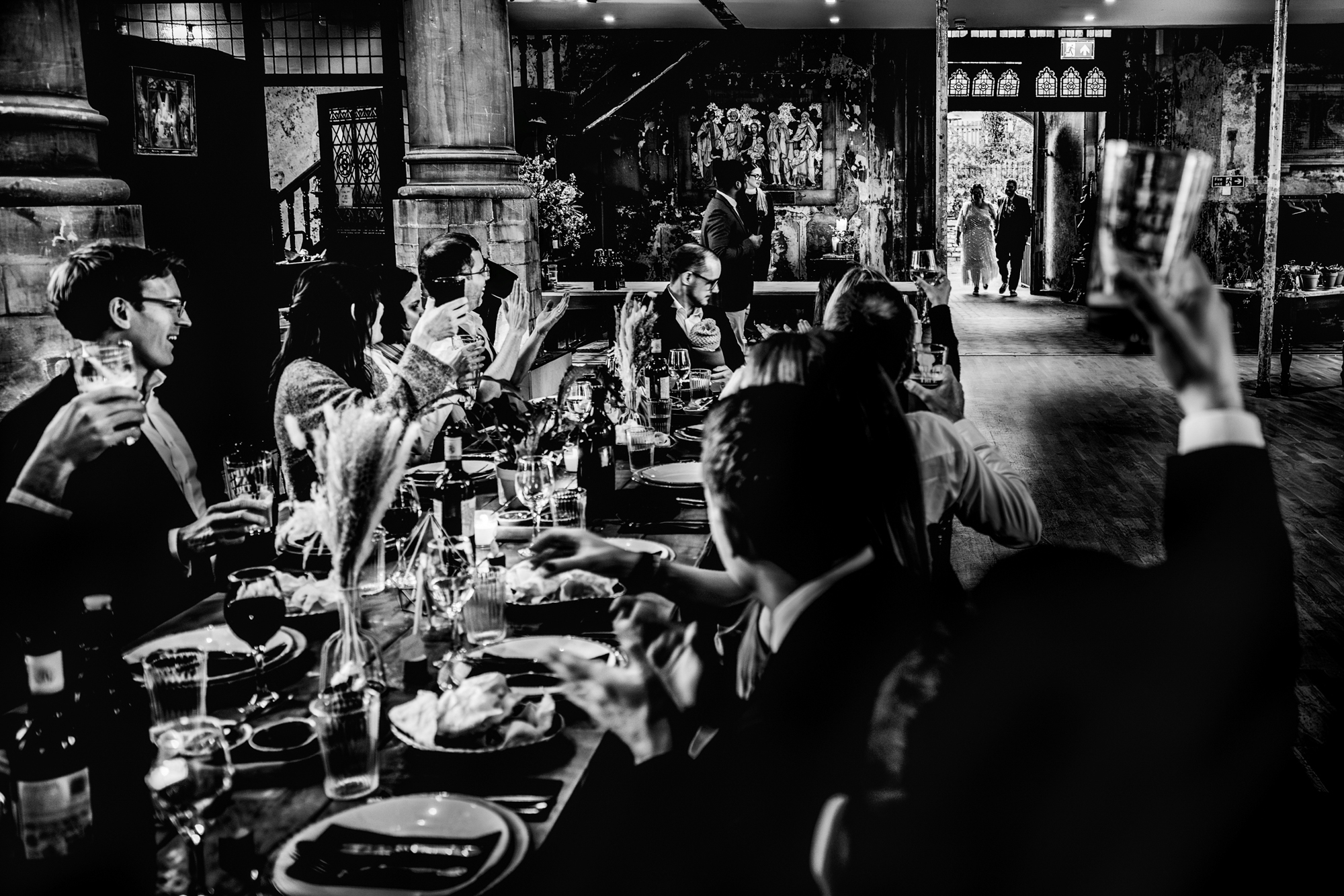 Couple walks into a rustic reception space as seated guests turn to applaud and raise drinks at the Mount Without