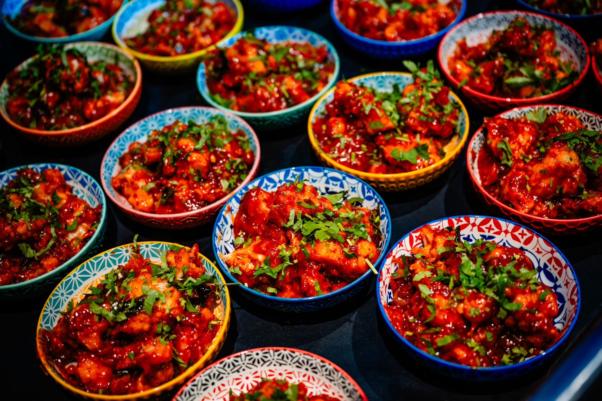Colorful bowls filled with a red, garnished curry are arranged closely together on a table.