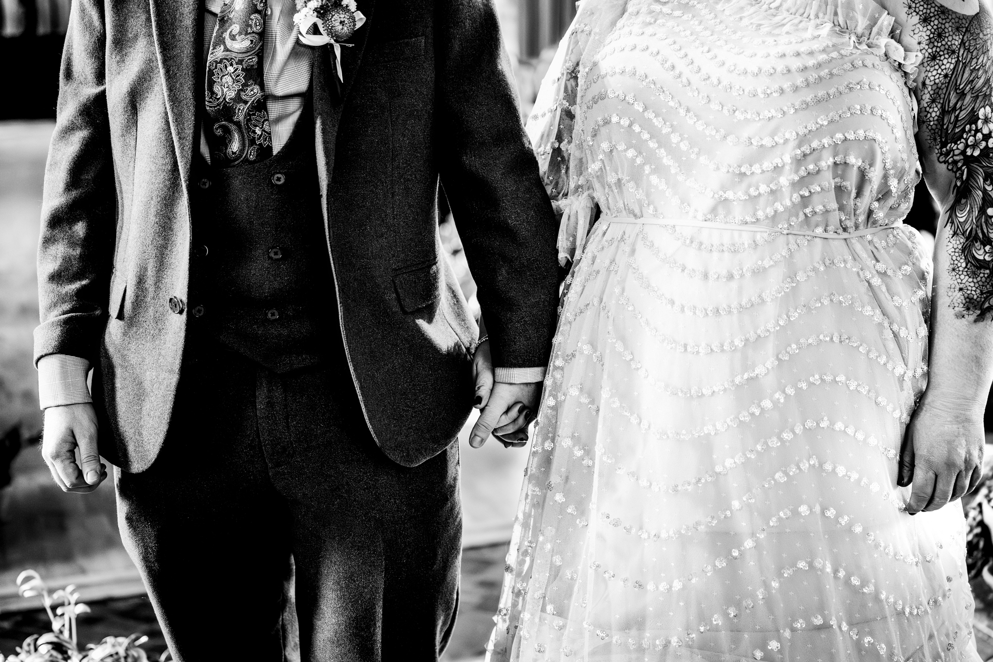 Close-up of couple holding hands during wedding ceremony with textured dress details.