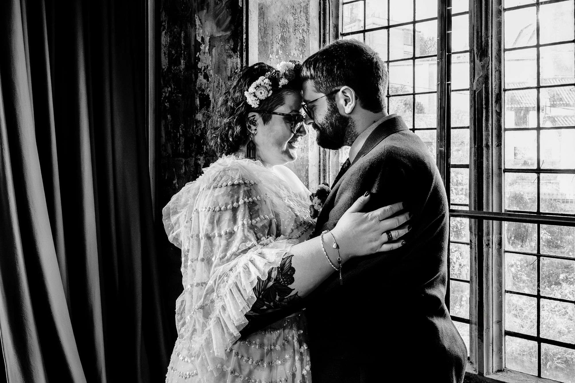 Intimate black and white portrait of couple touching foreheads by window light.