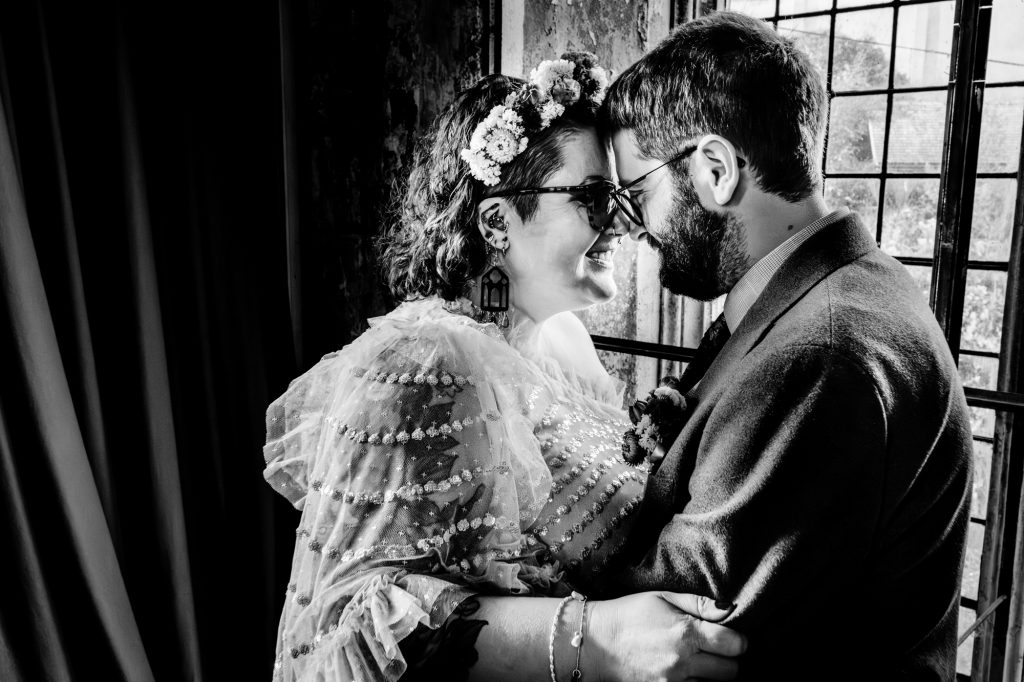 Intimate black and white portrait of couple touching foreheads by window light.