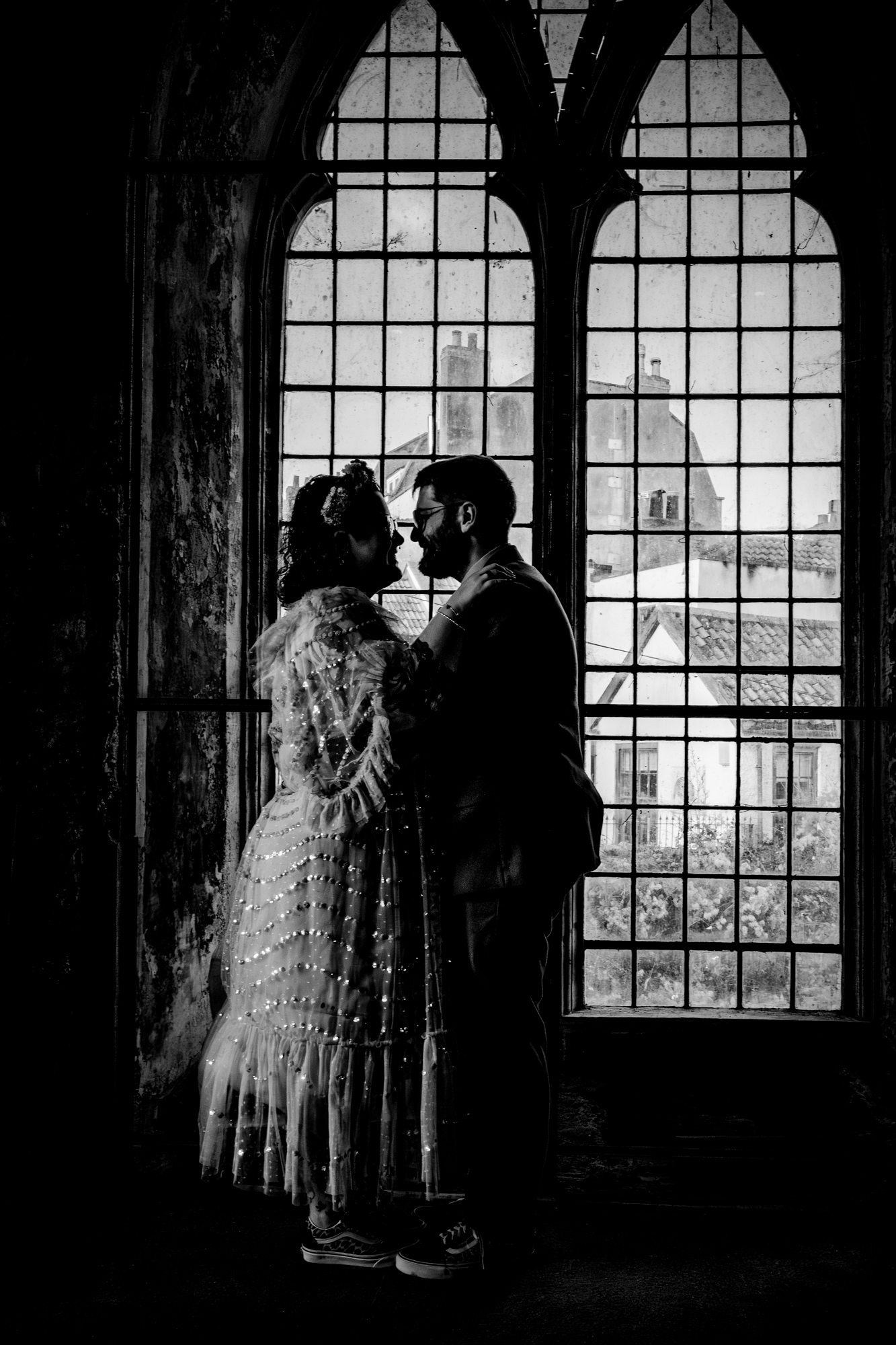 Silhouette of couple embracing in front of tall gothic windows inside Bristol wedding venue.