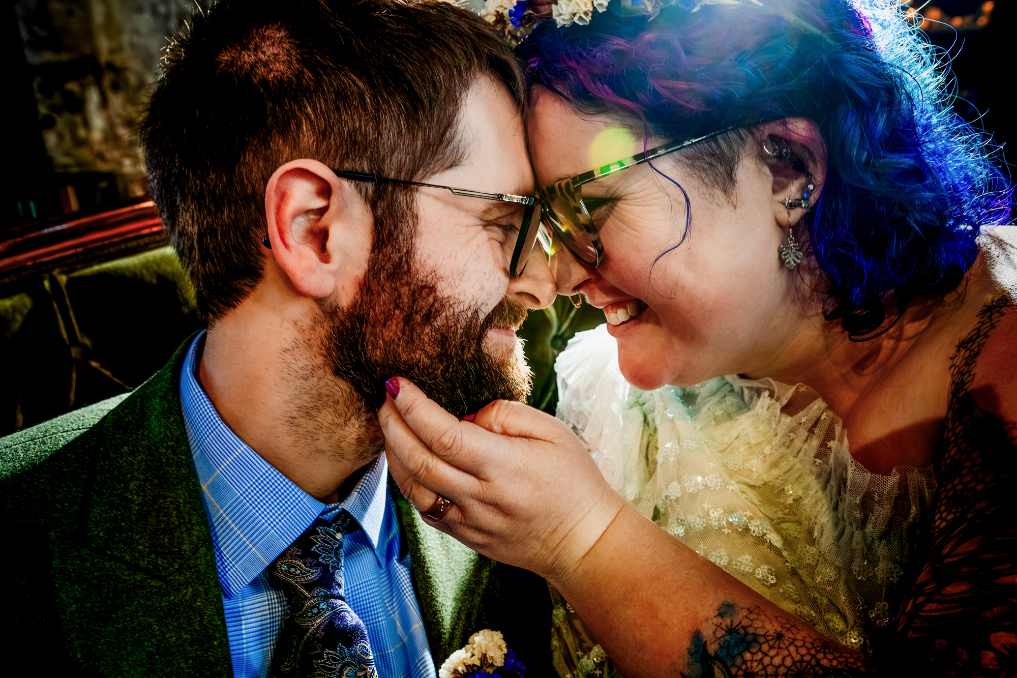 Close-up of the couple touching foreheads and smiling, with colorful lighting reflecting in their glasses.