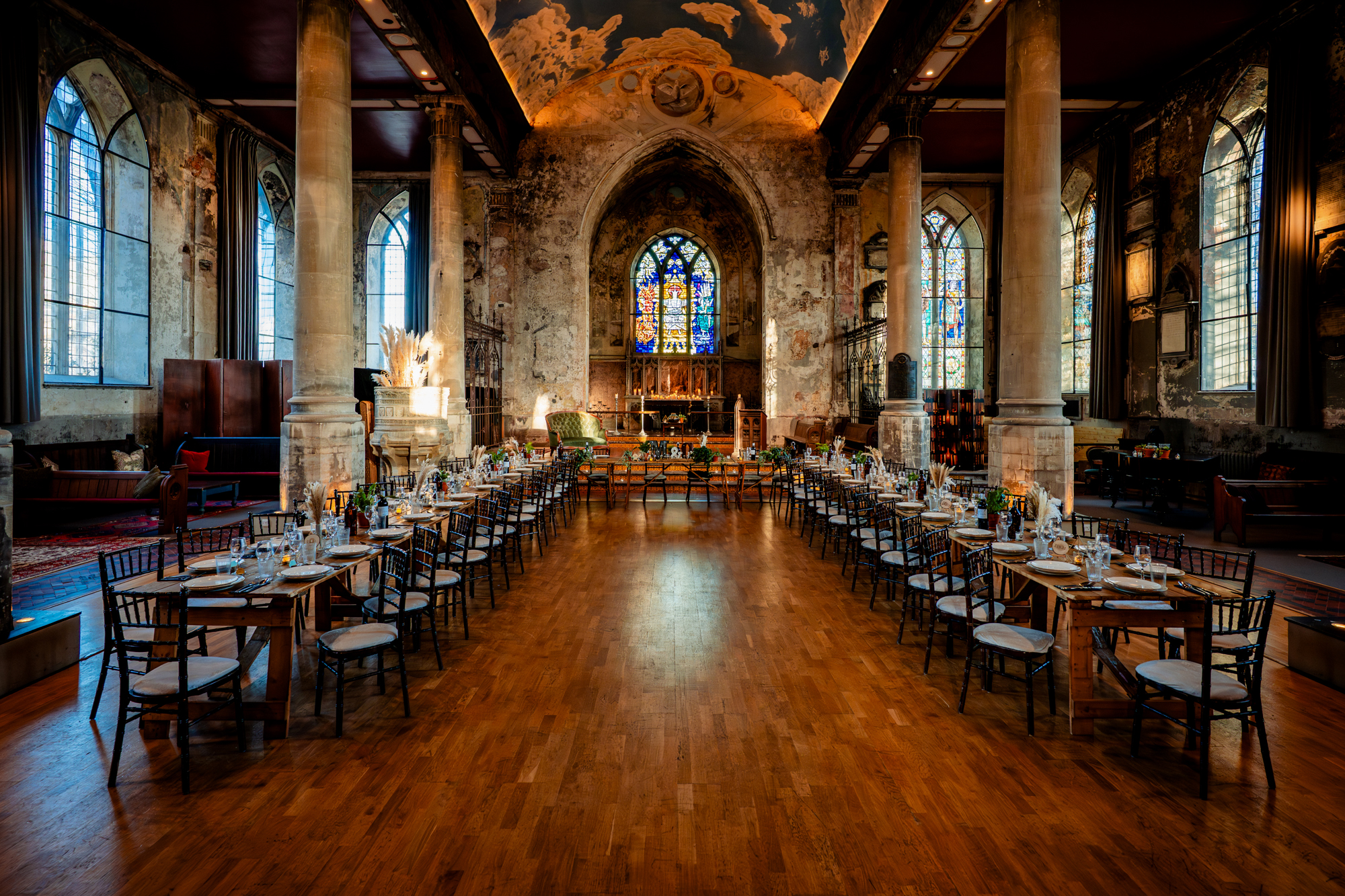 Wide view of a wedding reception layout inside a grand, aged church with long tables arranged symmetrically.