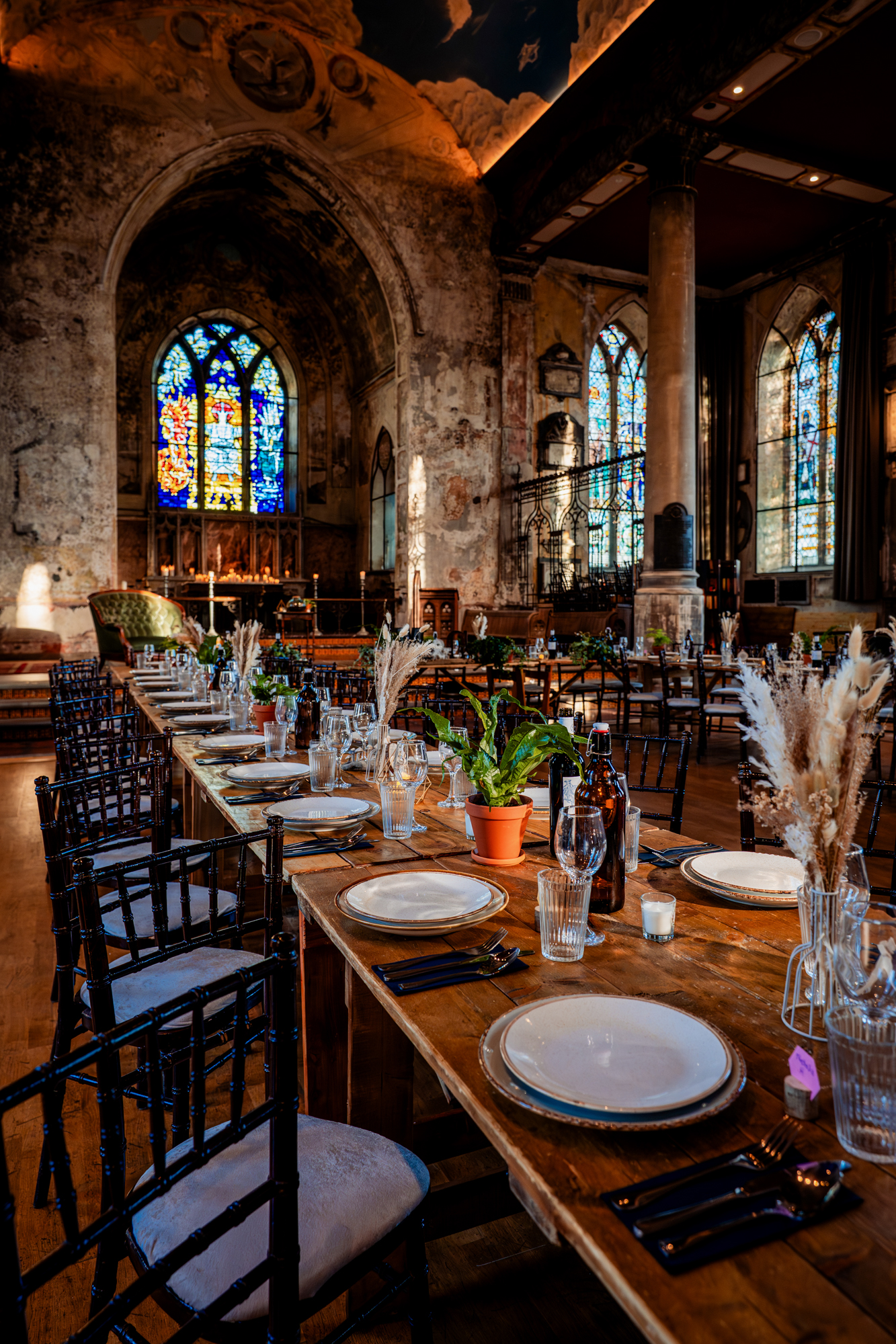 Angled view of banquet tables in a historic chapel with tall columns, stained glass, and warm ambient lighting.