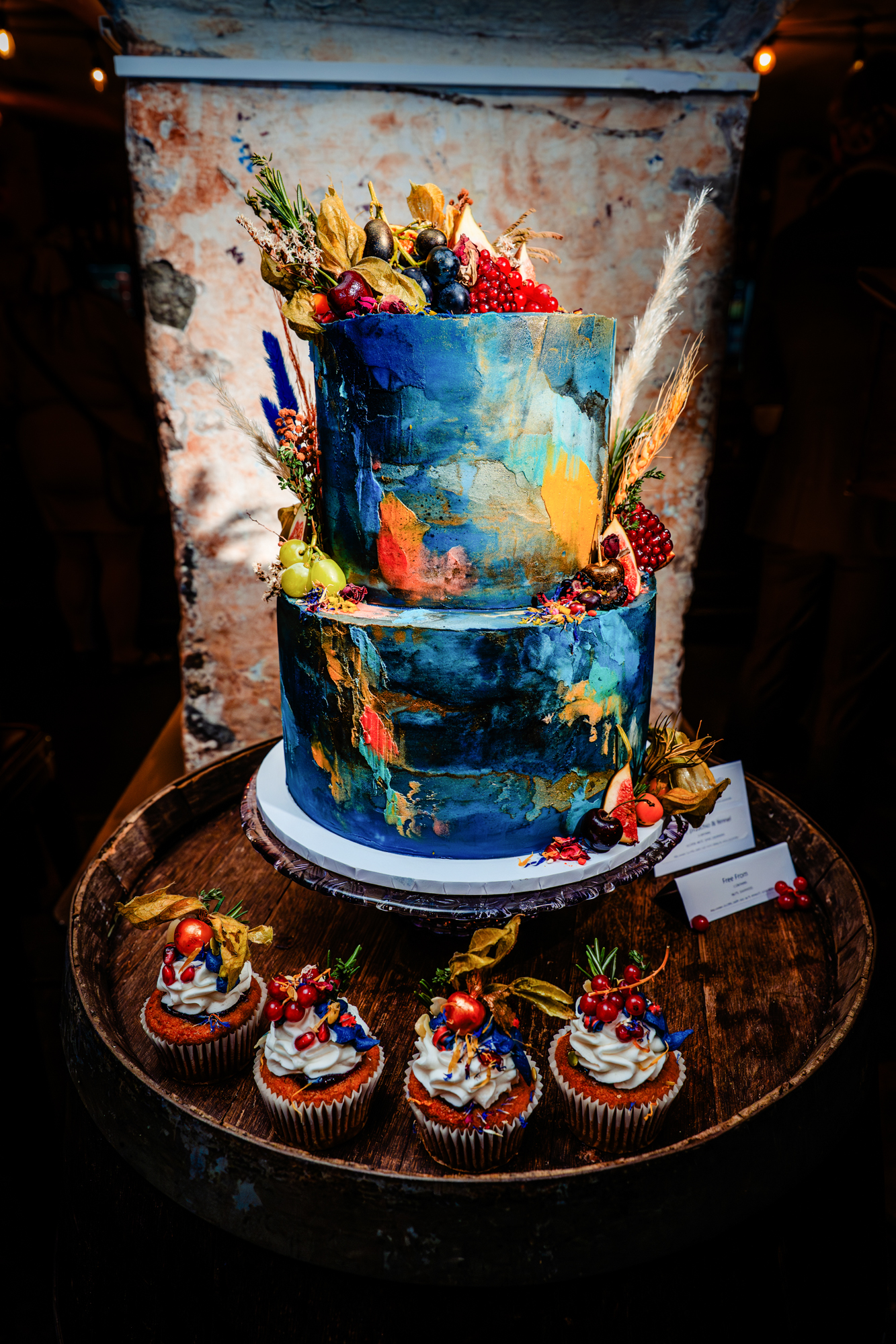 Alternate angle of the colorful wedding cake with matching cupcakes, styled with fruit, florals, and rustic décor.