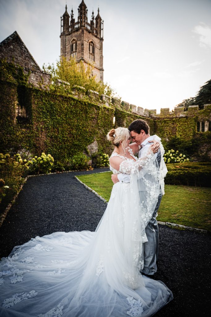 Emma and Steve are embracing in a historic courtyard at Thornbury Castle during golden hour.