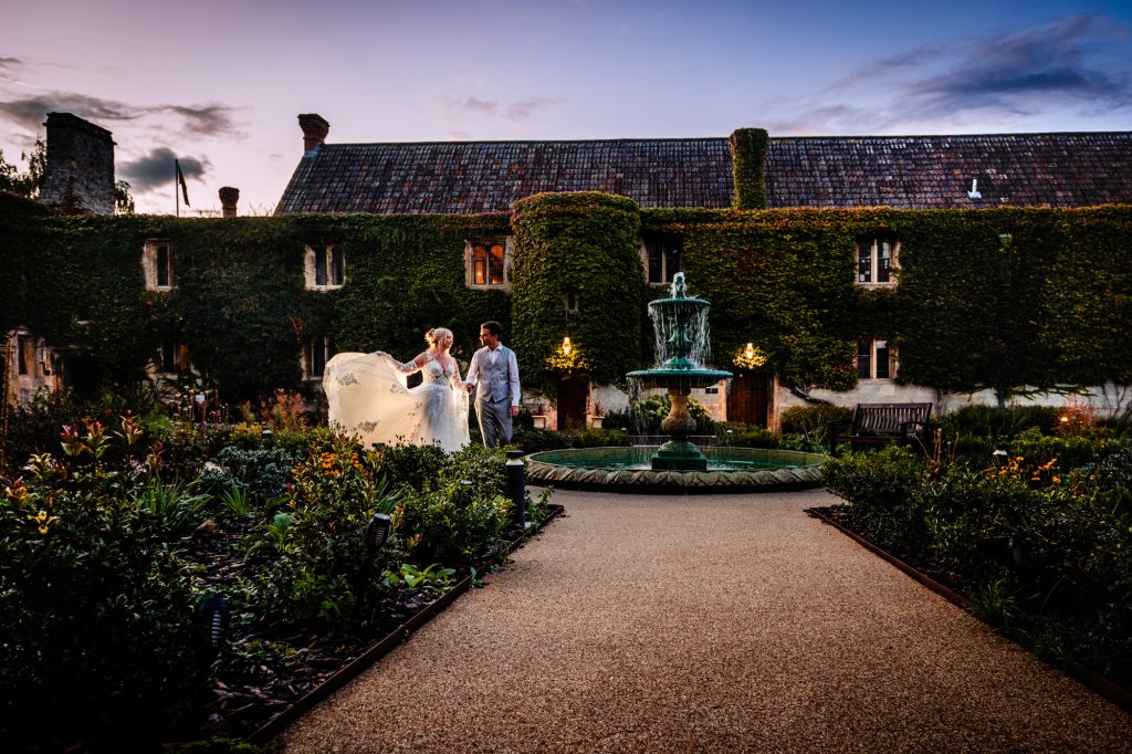 Bride lifting dress while walking beside a fountain, elegant garden wedding setting at Thornbury Hotel, Bristol.