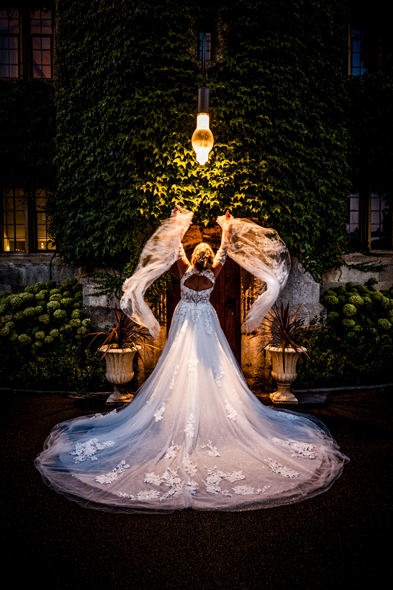 Bride spinning veil under warm light outside ivy-covered building, cinematic evening shot.