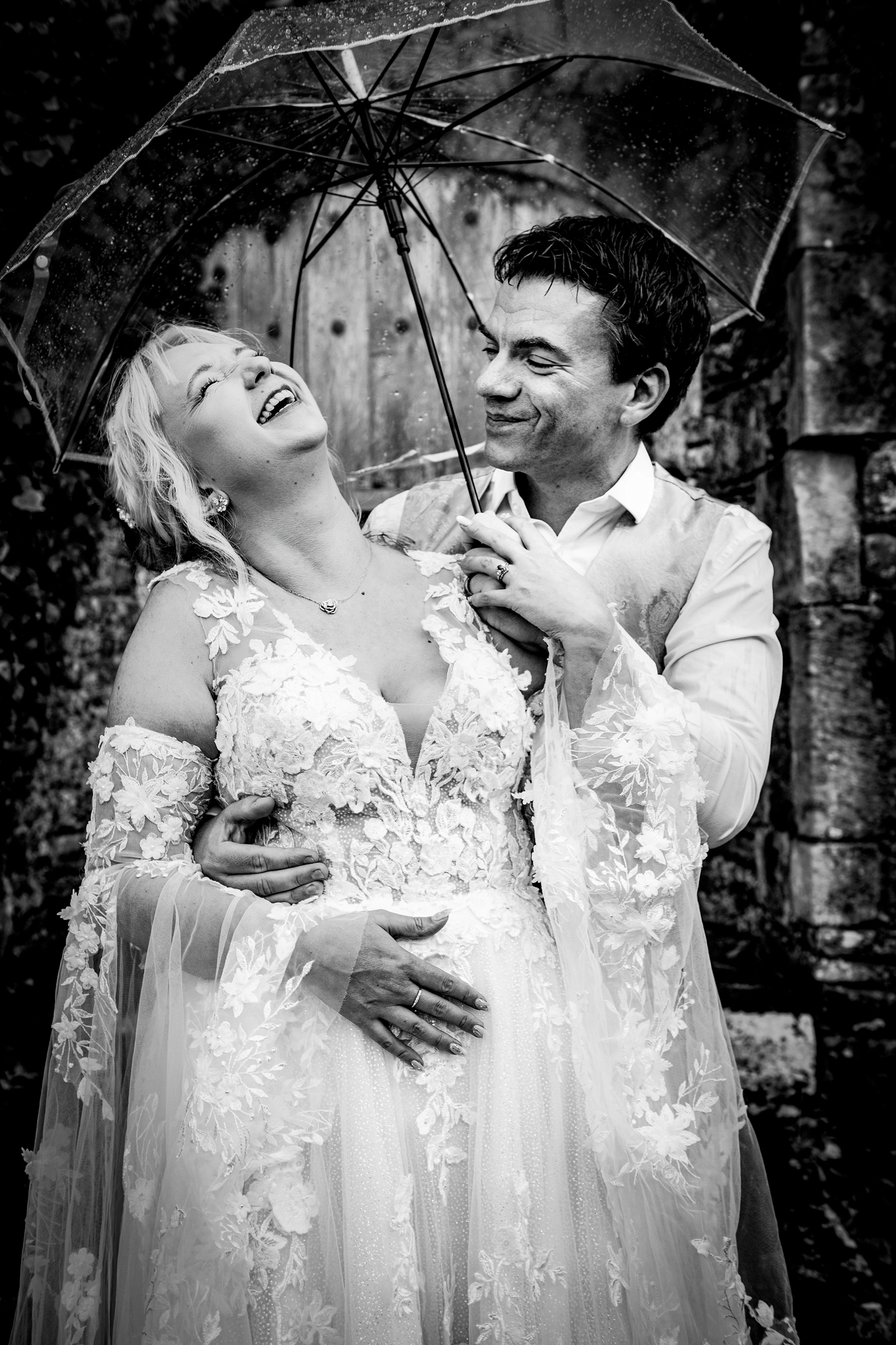 Emma laughing under a clear umbrella in rain during a candid moment at Thornbury Castle.